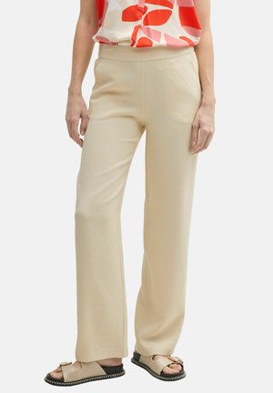 Beige wijde broek van een gestructureerde stof met een elastische tailleband, gecombineerd met zwarte sandalen en een kleurrijke geblokte top.