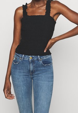 Czarny top na ramiączkach z marszczonym wykończeniem i falbankami na ramiączkach. Do tego niebieskie dżinsy o klasycznym kroju z delikatnym, wyblakłym wzorem.