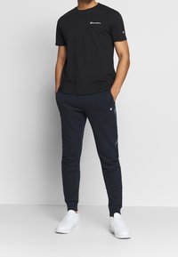 Sort bomulds t-shirt med et lille hvidt logo, parret med marineblå joggere med logo-detaljer og en slim fit, afsluttet med hvide sneakers.