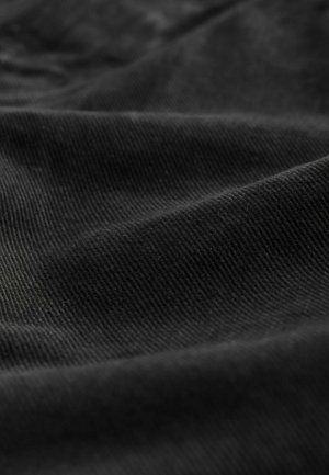 Zwart corduroy stof met een geribbeld patroon dat verschillende lichtreflecties vertoont, wat het gladde en iets pluizige oppervlak accentueert.