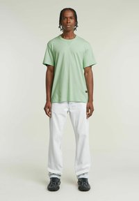 Maglietta verde menta a maniche corte, con scollo rotondo e vestibilità rilassata, abbinata a jeans denim chiari e sneakers nere testurizzate.