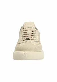 Beige Wildledersneaker mit runder Spitze, flachen Schnürsenkeln, strukturierten seitlichen Akzenten und einer gepolsterten Sohle, die ein dezentes, eingeprägtes Logo auf der Zunge aufweist.