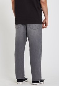 Pantalones de mezclilla gris con un corte relajado, que cuentan con dos bolsillos traseros y un diseño de pierna recta. Combinados con zapatillas negras.
