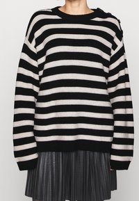 Czarny sweter w kremowe paski o dzianinowej teksturze, z okrągłym dekoltem i guzikami na ramionach. Długie rękawy.