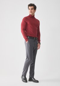 Pulover roșu cu guler înalt, pantaloni gri slim-fit, curea neagră și pantofi negri lustruiți. Textură fină, croială ajustată, estetică minimală.