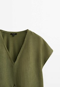 Top en lin vert olive à manches courtes avec un col en V profond et des finitions à bords francs au col et aux ourlets des manches.