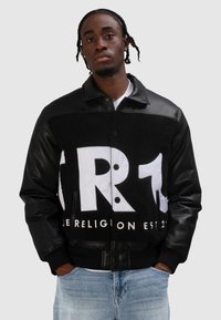 Czarna skórzana kurtka z polaru z białym graficznym logo; posiada zatrzaski z przodu, ściągacze na mankietach i kontrastującą fakturę.