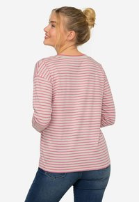 Camisa de manga larga a rayas en tejido ligero, con rayas horizontales en rosa y blanco, cuello redondo y corte relajado. Vaqueros visibles en la parte inferior.