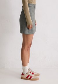 Szara wełniana spódnica o slim fit z rozkloszowanym dołem, zestawiona z beżowymi sneakersami z czerwonymi akcentami i białymi, prążkowymi skarpetami.