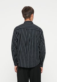 Zwart en blauw gestreepte shirt met lange mouwen, knoopmanchetten en een gebogen zoom. Beschikt over een ontspannen pasvorm en een klassieke kraag.