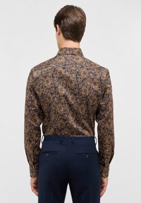 Een overhemd met lange mouwen in een donkerbruin paisleypatroon, met een puntige kraag en een gladde textuur, gecombineerd met marineblauwe broek met steekzakken.