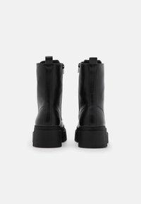 Bottes chelsea noires en cuir avec une semelle épaisse, des fermetures éclair arrière et une texture lisse ; conçues pour un ajustement sécurisé avec des languettes de tirage.