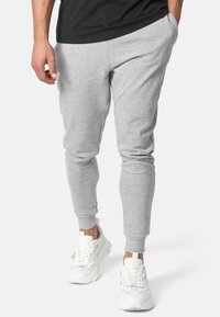 Graue Sweatpants aus einem Baumwollmix, eng zulaufender Schnitt, mit seitlichen Taschen und elastischen Bündchen, kombiniert mit weißen Turnschuhen.