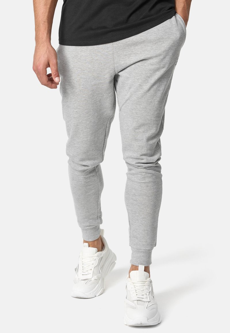 Graue Sweatpants aus einem Baumwollmix, eng zulaufender Schnitt, mit seitlichen Taschen und elastischen Bündchen, kombiniert mit weißen Turnschuhen.