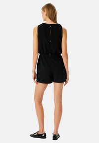 Mono negro sin mangas con cintura ajustada, cierre de botones en la parte posterior y diseño de pantalones cortos. Tejido suave con un ajuste cómodo.