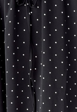 Czarna tkanina w białe kropki, gładka w dotyku, z detalem w postaci sznurka przy dekolcie oraz swobodnymi fałdami.