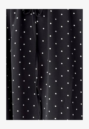 Czarna tkanina w białe kropki, gładka w dotyku, z detalem w postaci sznurka przy dekolcie oraz swobodnymi fałdami.