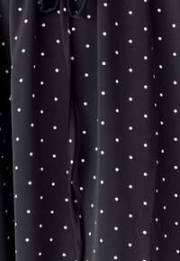 Schwarzer Stoff mit weißen Polka-Punkten, glatte Textur, mit einer Kordelzug-Detail am Ausschnitt und fließenden Drapierungen.