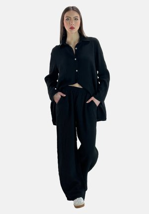 Sort, tekstureret stofoutfit bestående af en langærmet skjorte med knapper og løstsiddende bukser, parret med hvide sneakers.