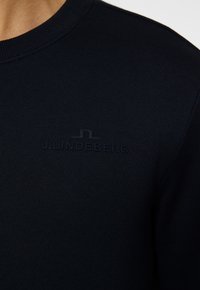 Marinblå sweatshirt med ribbad halsringning och präglad logotyp "J. LINDEBERG" i en ton-i-ton nyans, tillverkad av mjukt, hållbart tyg.