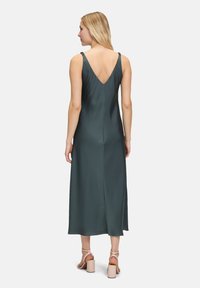 Robe satin mi-longue, vert foncé, avec un dos en V, des fines bretelles et une texture lisse, assortie à des sandales à talons блокs de couleur claire.