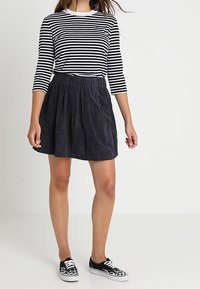Top de manga larga a rayas en blanco y negro combinado con una falda plisada azul marino. Completado con zapatillas slip-on a cuadros en blanco y negro.