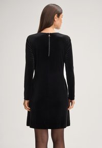 Schwarzes Samtkleid mit langen Ärmeln, Reißverschluss auf der Rückseite und taillierter Passform. Glatte Textur, knielang, minimalistischer Stil.