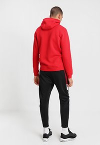 Rode hoodie met een textuur oppervlak en verstelbare koord, gecombineerd met zwarte taps toelopende broek met zijpanele en zakken.