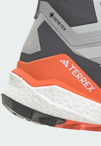 Szare i czarne tekstylne sneakersy z pomarańczowymi akcentami, z teksturowaną powierzchnią, wyściełaną białą podeszwą środkową oraz logo GORE-TEX.
