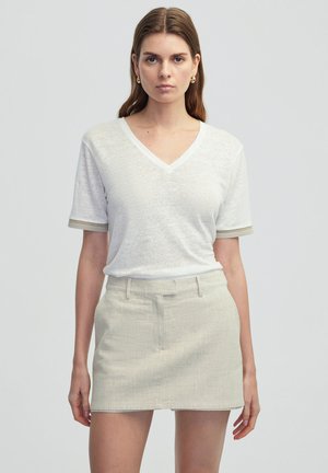 T-shirt blanc à col en V, en tissu texturé et à manches courtes, associé à une mini-jupe beige clair texturée. Les deux sont simples et bien taillés.