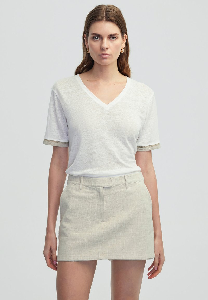 Witte V-hals T-shirt van gestructureerde stof met korte mouwen, gecombineerd met een lichtbeige gestructureerde minirok. Beide zijn eenvoudig en op maat gemaakt.