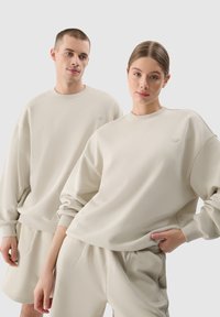 Beige környakú pulóverek laza szabással és bordás mandzsettákkal, párosítva hozzá illő rövidnadrággal. Puha, textúrált anyag finom márkajelzéssel.