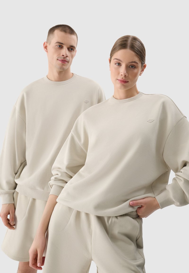 Beige környakú pulóverek laza szabással és bordás mandzsettákkal, párosítva hozzá illő rövidnadrággal. Puha, textúrált anyag finom márkajelzéssel.