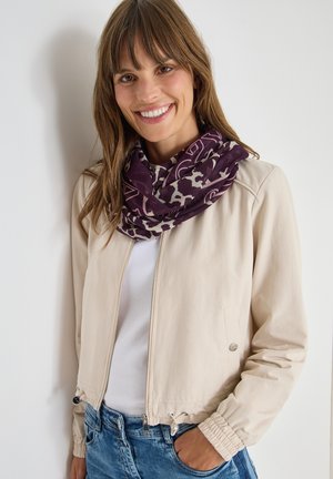 Jacket bomber beige con zip frontale, polsini elastici e orlo con cordino. Abbinata a una sciarpa modellata viola e bianca.