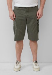 Olive greenowe szorty cargo z bocznymi kieszeniami, wykonane z bawełnianej tkaniny. Płaski przód, długość do kolan, uzupełnione białymi sneakersami.