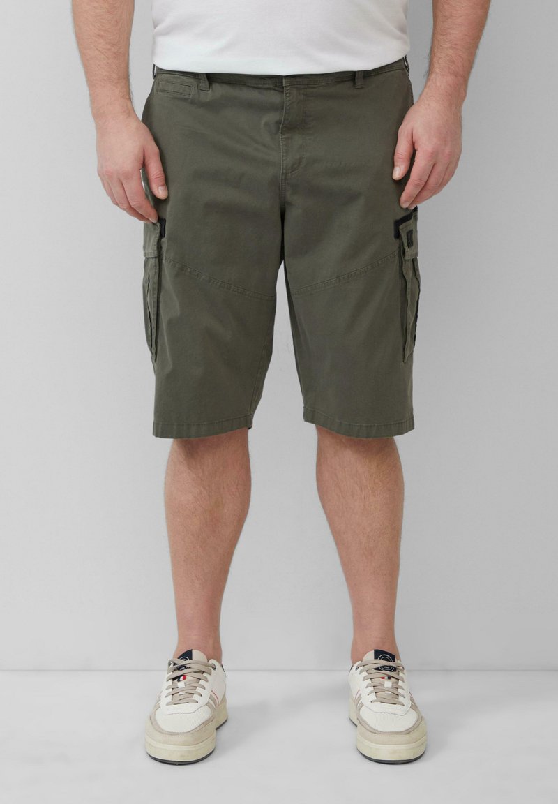 Olive greenowe szorty cargo z bocznymi kieszeniami, wykonane z bawełnianej tkaniny. Płaski przód, długość do kolan, uzupełnione białymi sneakersami.