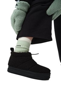 Czarne futrzane buty z teksturowanym cholewką, okrągłym noskiem i czarną gumową podeszwą. W połączeniu z jasnoszarymi skarpetkami w prążki i czarnymi spodniami.