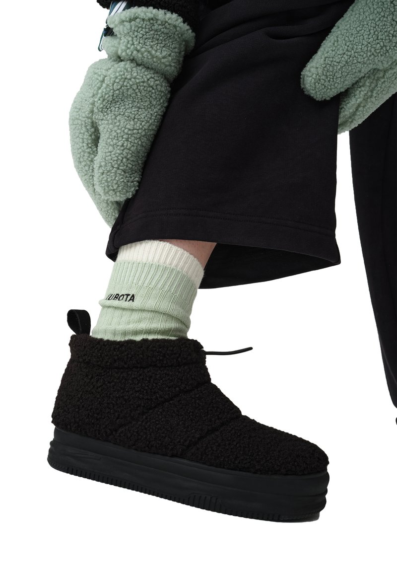Czarne futrzane buty z teksturowanym cholewką, okrągłym noskiem i czarną gumową podeszwą. W połączeniu z jasnoszarymi skarpetkami w prążki i czarnymi spodniami.