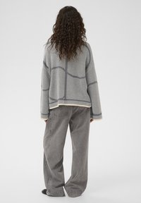 Pull gris en tricot avec motifs géométriques, manches longues et coupe ample. Associé à un pantalon gris taille haute à jambes larges.