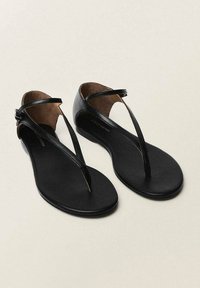 Black leather sandals with a flat sole, featuring a T-strap design and an adjustable ankle strap. Smooth texture and minimalistic style.