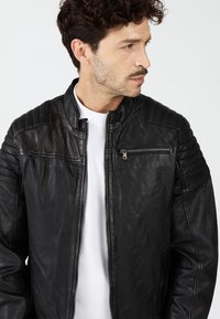 Zwarte leren jas met een naadloos ontwerp, ritszak op de borst en gesteppte schouderaccenten. Soepele textuur met een klassieke pasvorm.