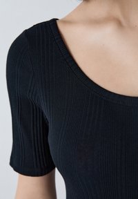 Top noir à côtes avec un col large et des manches courtes, fabriqué dans un matériau extensible avec une texture lisse et un léger brillant.