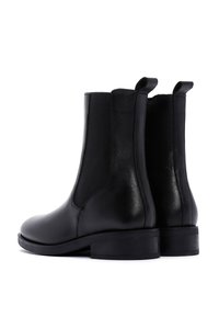 Bottines Chelsea en cuir noir avec panneaux latéraux élastiques et languettes. Texture lisse, talon bas, design épuré et bout arrondi.