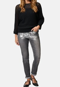 Pull noir en maille ajourée avec manches larges, associé à un jean skinny métallique argenté et des ballerines noires avec une bride autour de la cheville.