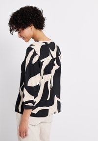 Schwarze und cremefarbene Bluse mit abstraktem Muster, dreiviertelärmlig und mit rundem Ausschnitt, die über einen Knopf am Ärmelabschluss verfügt.