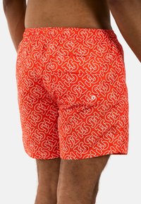 Costumi da bagno rossi con un motivo geometrico bianco, vita elasticizzata e tasca posteriore. Realizzati in materiale leggero e a asciugatura rapida.
