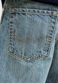 Zadní kapsa modrých džínů z denimu s oranžovým šitým zakřiveným vzorem, zobrazující texturu a vybledlé vertikální linie v látce.