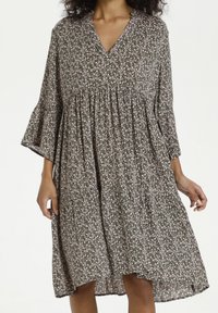 Grünes Blumenkleid mit V-Ausschnitt und ausgestellten Ärmeln, ausgestattet mit einem gerafften Taillenteil und leichtem Stoff. Das Muster beinhaltet kleine rosa Blumen.