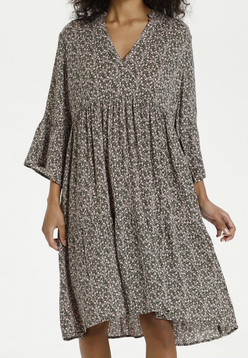 Grünes Blumenkleid mit V-Ausschnitt und ausgestellten Ärmeln, ausgestattet mit einem gerafften Taillenteil und leichtem Stoff. Das Muster beinhaltet kleine rosa Blumen.