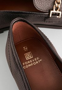 Crni teksturirani loafers s zlatnim lancem kao naglaskom. Unutrašnjost ima smeđu podstavu i otisnuti logo. Veličina označena kao 40.
